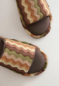 Paar gemütliche Hausschuhe mit mehrfarbigem Zickzack-Strickmuster in Braun-, Grün-, Beige- und Orangetönen auf grauen Innensohlen.