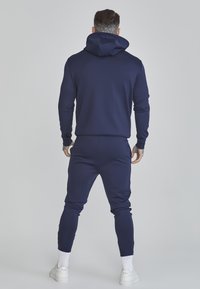 Navy blue, cotton blend tracksuit featuring a hooded sweatshirt and tapered pants. Smooth texture with ribbed cuffs and ankle hems.