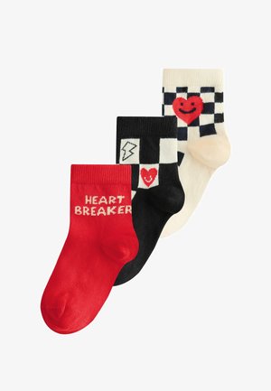 Three pairs of socks: red with "HEART BREAKER" text, black with checkered pattern and smiling heart, cream with checkered pattern and large smiling heart.