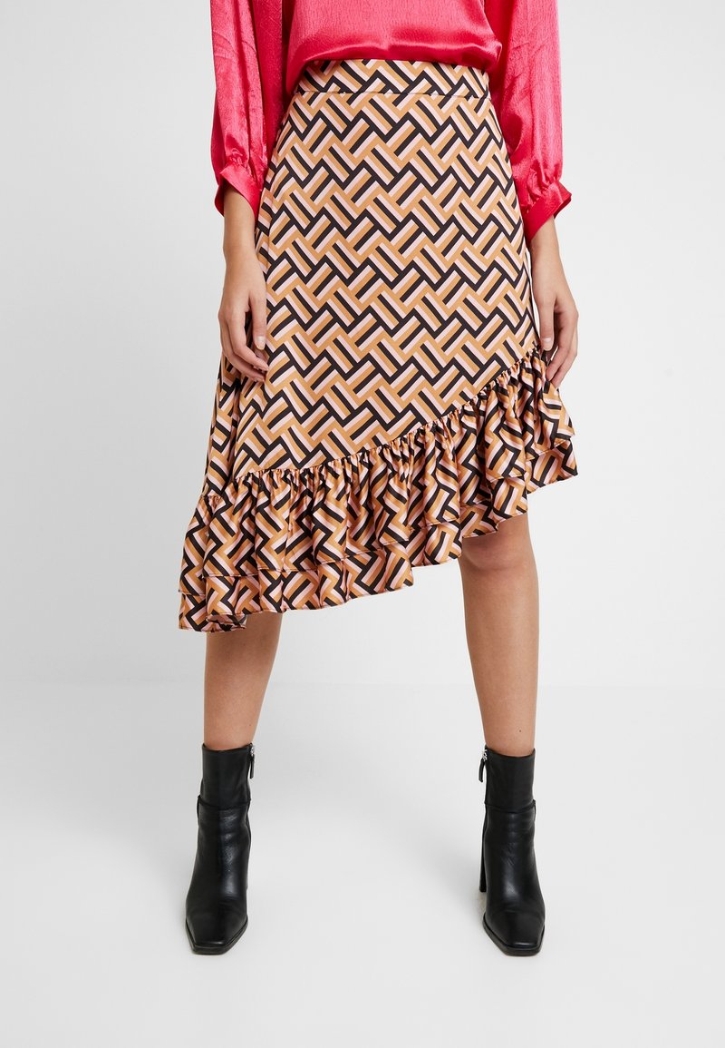 Jupe asymétrique au motif zigzag orange, rose et noir avec un ourlet à volants. Portée avec des bottines noires. Fabriquée en tissu léger.