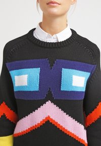 Schwarzer Strickpullover mit geometrischen Mustern. Verfügt über leuchtend blaue, weiße, lila, rosa und orangefarbene Akzente. Rundhalsausschnitt.