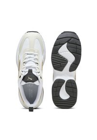 Vit och beige Puma-sneaker visad uppifrån med snören och sula med svart mönster mot vit bakgrund.