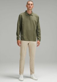 Zielona, długosleeve polo z kołnierzykiem i zapięciem na guziki, w połączeniu z jasnobeżowymi, slim-fit spodniami i białymi trampkami, prezentowane przez mężczyznę.