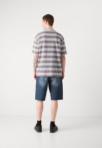 Grå og brun stribet kortærmet skjorte parret med blå denimshorts. Skjorten har en afslappet pasform, og shortsene er knælange.