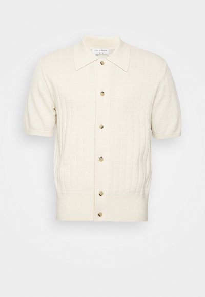Šortinio rankovių kreminio spalvos cardigan'o, pasižyminčio reliefiniu tekstūru, penkių mygtukų užsegimu ir smailiu apykaklė. Medžiaga atrodo minkšta ir glotni.