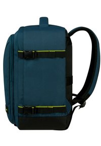 Zaino in tessuto blu con accenti neri. Presenta due spalline regolabili, una maniglia superiore e fibbie laterali. Esterno testurizzato, forma rettangolare.