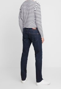 Mörkblå denimjeans med slim fit, med bakfickor och ljusa sömmar, kombinerade med en vit och marinrandig långärmad skjorta.