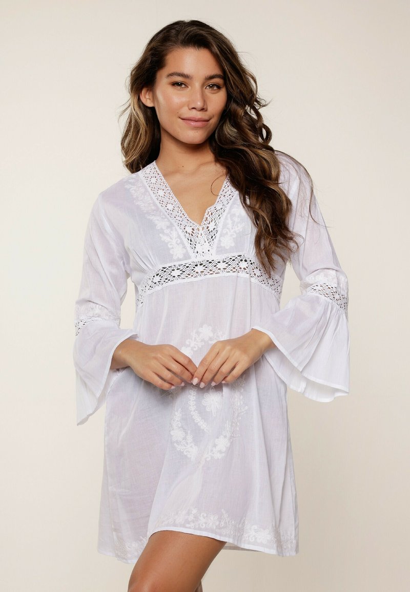 Vestido túnica blanco hecho de una tela ligera, con escote en V, acentos de encaje y mangas acampanadas con detalles de bordado floral.