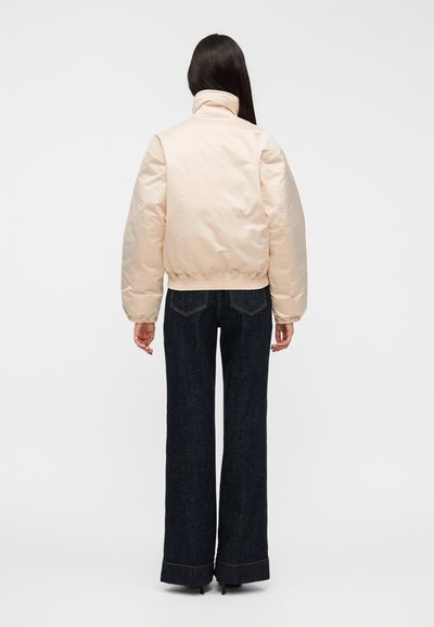 Otepľovaná, svetloružová bunda s vysokým golierom a elastickým lemom, doplnená rovnými tmavomodrými džínsami s kontrastným prešívaním.