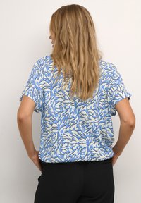 Blusa a maniche corte in tessuto azzurro chiaro con un motivo ispirato alle piante in bianco e nero. Vestibilità ampia con orlo arrotondato.
