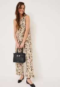 Haut sans manches beige et pantalon large avec un motif abstrait noir. Sac à main noir avec des poignées courtes et des détails en argent. Ballerines noires.