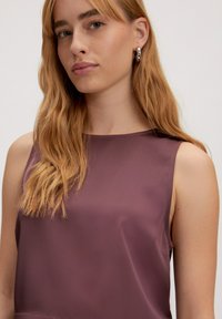 Paarse mouwloze top met een gladde, glanzende textuur, ronde halslijn en een eenvoudig ontwerp. Model toont de pasvorm en de val van het kledingstuk.