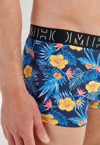 Boxer shorts con estampado floral sobre un fondo azul oscuro, con flores amarillas y rosas, hojas verdes y una cinturilla elástica negra.
