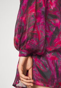 Blusa floreale in tonalità di rosa e nero, con tessuto trasparente, maniche a palloncino e dettagli in perline testurizzate lungo il motivo.