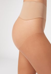 Collants de compression beiges avec une texture lisse, une taille haute et une finition transparente sur les jambes, présentés sur un fond clair.