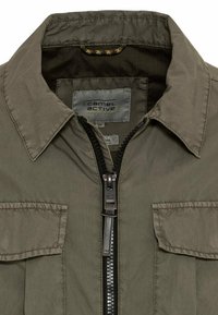 Col et section de fermeture éclair d'une veste Camel Active vert olive avec poches à rabat et étiquette de marque visible à l'intérieur du col.