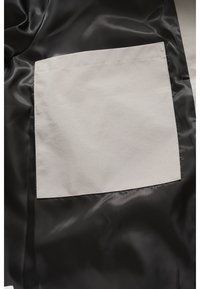 Schwarzer Satinstoff mit einer großen grauen aufgesetzten Tasche. Die Tasche ist rechteckig, matt und hat gerade Nähte entlang der Kanten.