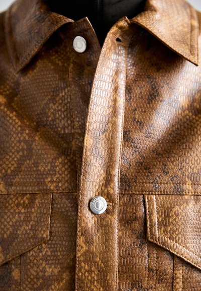 Veste en cuir synthétique marron avec un motif serpent, dotée d'un col pointu, de boutons pression et de poches poitrine. Texture lisse et coutures détaillées.