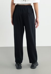 Black, loose-fitting sweatpants made of soft fabric. Features an elastic waistband and a single back pocket.
