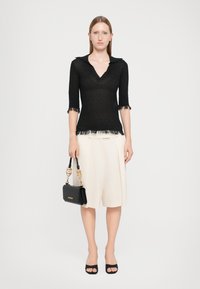 Schwarzes Stricktop mit V-Ausschnitt und kurzen Ärmeln, mit ausgefransten Säumen. Kombiniert mit cremefarbenen, gefältelten Shorts und einer kleinen schwarzen Handtasche.