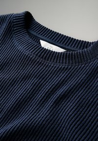 Suéter de punto acanalado azul marino con cuello redondo y etiqueta blanca visible dentro del cuello.