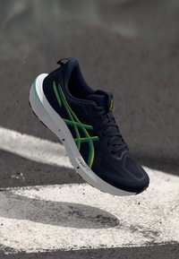 Scarpa da corsa navy con tomaia testurizzata, dettagli gialli e verdi e suola bianca. Design leggero con lacci e logo.