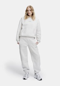 Ljusgrå sweatshirt och matchande sweatpants av mjukt tyg. Sweatshirten har en framficka och varumärkets text i en diskret tryck.