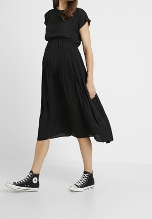Robe midi plissée noire à manches courtes et taille élastique, associée à des baskets montantes noires. Design simple et fluide.