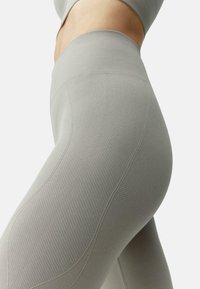 Šviesiai pilkos kelnės su raižyta tekstūra, aukštu liemeniu ir panelėmis šonuose. Sukurtos patogumui ir lankstumui.