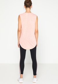 Haut rose sans manches avec ourlet arrondi, associé à des leggings noirs avec des bandes latérales roses. Des chaussures de sport complètent la tenue.