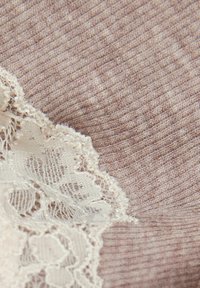 Ljust brunt tyg med en ribbad struktur, med en kant av intrikat vit spets som ger en delikat detalj till materialet.