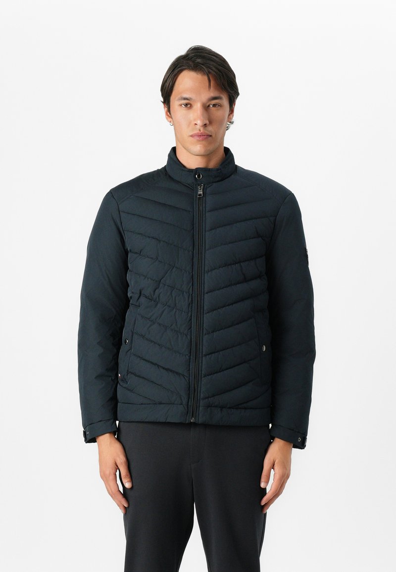 Czarna pikowana kurtka z wysokim kołnierzem, przednim zamkiem błyskawicznym i ukośnym przeszyciem. Posiada mankiety na zatrzaski i wykonana jest z teksturowanej tkaniny.