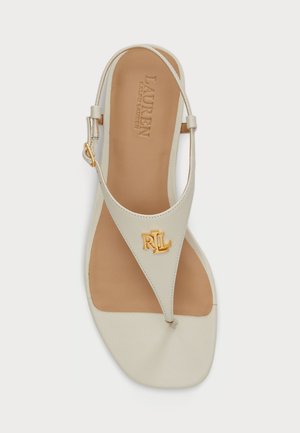 Sandały z paskiem w kolorze brązowym i kremowym, z teksturowaną cholewką, złotym akcentem z logo oraz regulowanym paskiem wokół kostki. Płaska podeszwa z gładką wkładką.