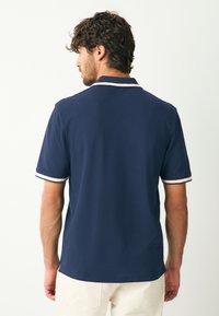 Tumesinine polosärk, millel on krae valgete ja roosade triipudega, lühikesed varrukad ja külgedel lõhik. Sile kangas ja lõdvestunud lõige.