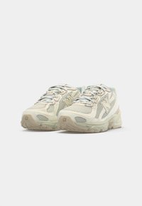 Scarpe da corsa leggere in rete crema e verde pallido con suola in gomma, caratterizzate da una tomaia testurizzata, punta rinforzata e logo prominente.