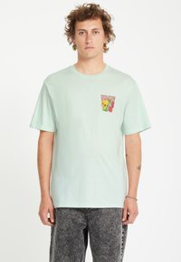 Camiseta de algodón verde menta con cuello redondo y mangas cortas; presenta un colorido diseño de bolsillo gráfico con texto y elementos florales.