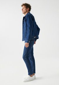 Chaqueta de denim y jeans en azul oscuro, con un corte clásico, cierre de botones y detalles de costura sutiles, combinados con zapatillas blancas.