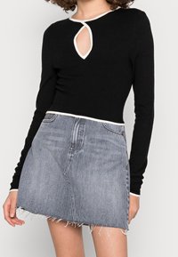 Svart långärmad topp med utskuren halsringning, i kombination med en ljusblå jeanskjol med fransar. Toppen har vit kant vid halsringningen.