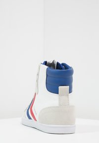 Pantofii sport înalți cu pânză albă, accente din piele albastră, detalii din suede gri și dungi roșii. Prezintă guler căptușit și talpă din cauciuc alb.