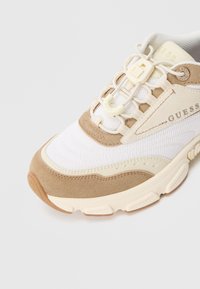 Λευκό και μπεζ αθλητικό παπούτσι Guess με πάνελ από δίχτυ και σουέτ, ελαστικά κορδόνια με κουμπώματα και χοντρή υφή στη σόλα.