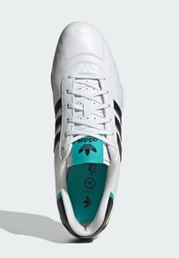 Biele atletické topánky s čiernymi prúžkami, kožným zvrškom a tyrkysovými akcentmi na jazyku. Má guľaté šnúrky a polstrovaný interiér.