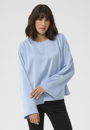 Hellblaue Bluse mit langen Ärmeln und rundem Ausschnitt, glatter Textur und weit auslaufenden Ärmeln; kombiniert mit schwarzen Hosen.