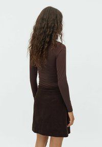 Brun ribbet langærmet top parret med en kort, tekstureret fløjlssy. Outfittet har slanke silhuetter og en glat finish.