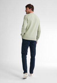 Sudadera verde claro con un acabado texturizado, cuello redondo y puños acanalados, combinada con pantalones azul marino oscuros y zapatillas blancas.