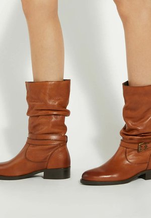 Bottes en cuir marron à la cheville avec un design décontracté, présentant un talon bas, un accent de boucle et une texture lisse.