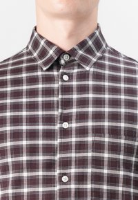 Checked shirt in dark burgundy and white, featuring a button-down collar, front pocket, and smooth cotton texture with contrasting buttons.