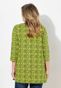 Grøn- og gulmønstret tunika med trekvartærmer, der har et blomsterdesign og lige snit, parret med mørk denim.