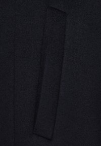 Czarna tkanina wełniana z widocznym pionowym szwem i prostokątnym detalem w klapie, tworząca teksturową powierzchnię bez wzorów.