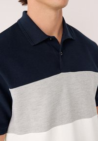 Marineblaues und graues Polohemd mit Streifen und strukturiertem Stoff, ausgestattet mit einem klassischen Kragen und einer Knopfleiste mit drei Knöpfen.