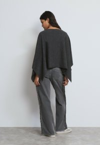 Poncho gris ligero con un ajuste amplio, que presenta un dobladillo recto y mangas anchas. Combinado con jeans gris de pierna ancha adornados con flecos.